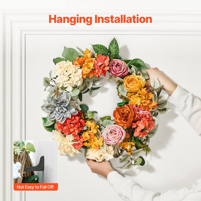 Artificial hydrangea rose wreath in vibrant fall colors being hung on white wall for decoration